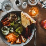 Top view of healthy salad with assorted vegetables and toasted bread placed on wooden table with exotic fresh drink and cutlery